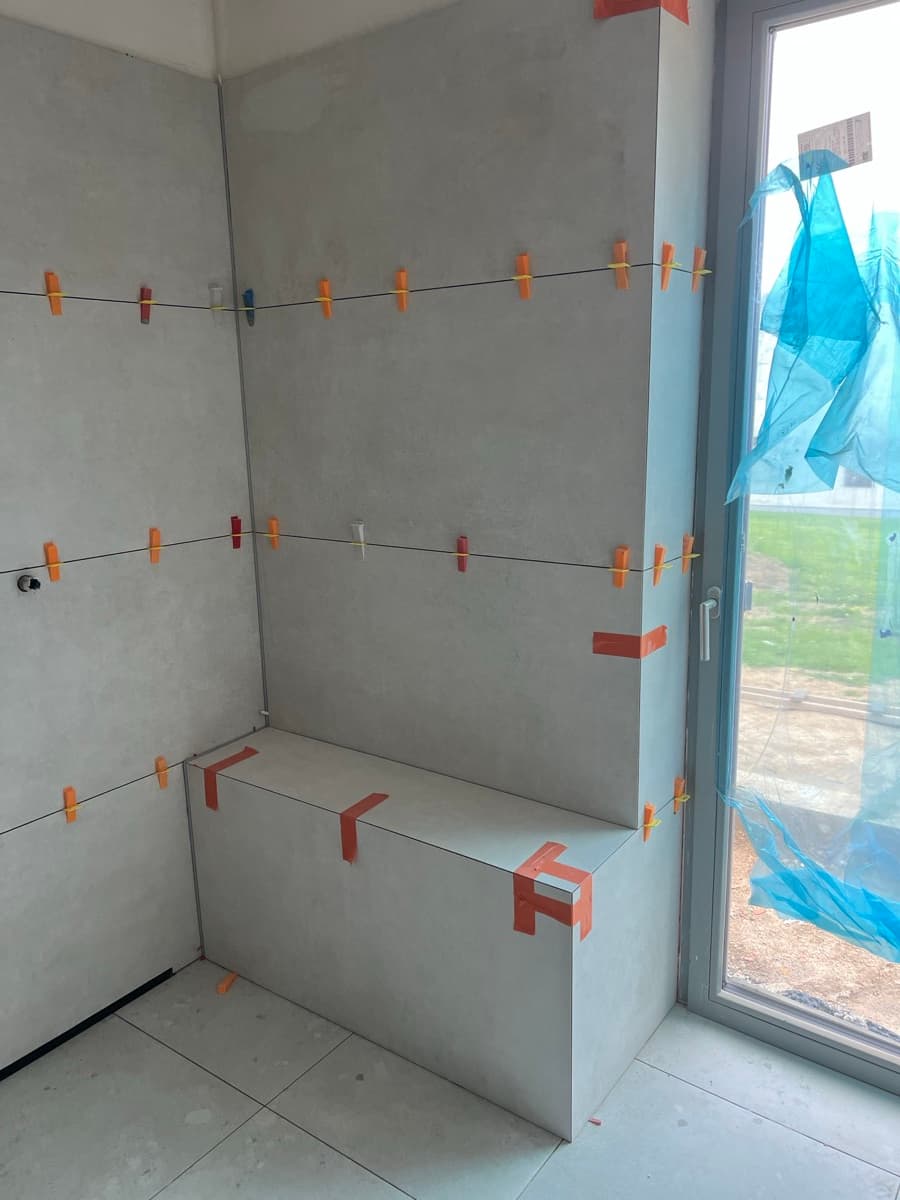 Zděná lavice ve sprchovém koutě během pokládky — nivelační spony a fixace desky — realizace OBK, Ostrava