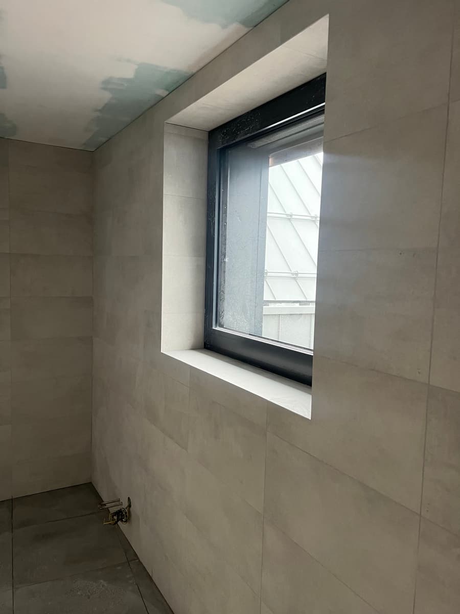 Obložené ostění okna v koupelně — velkoformátový obklad a parapet z dlažby — realizace OBK, Ostrava